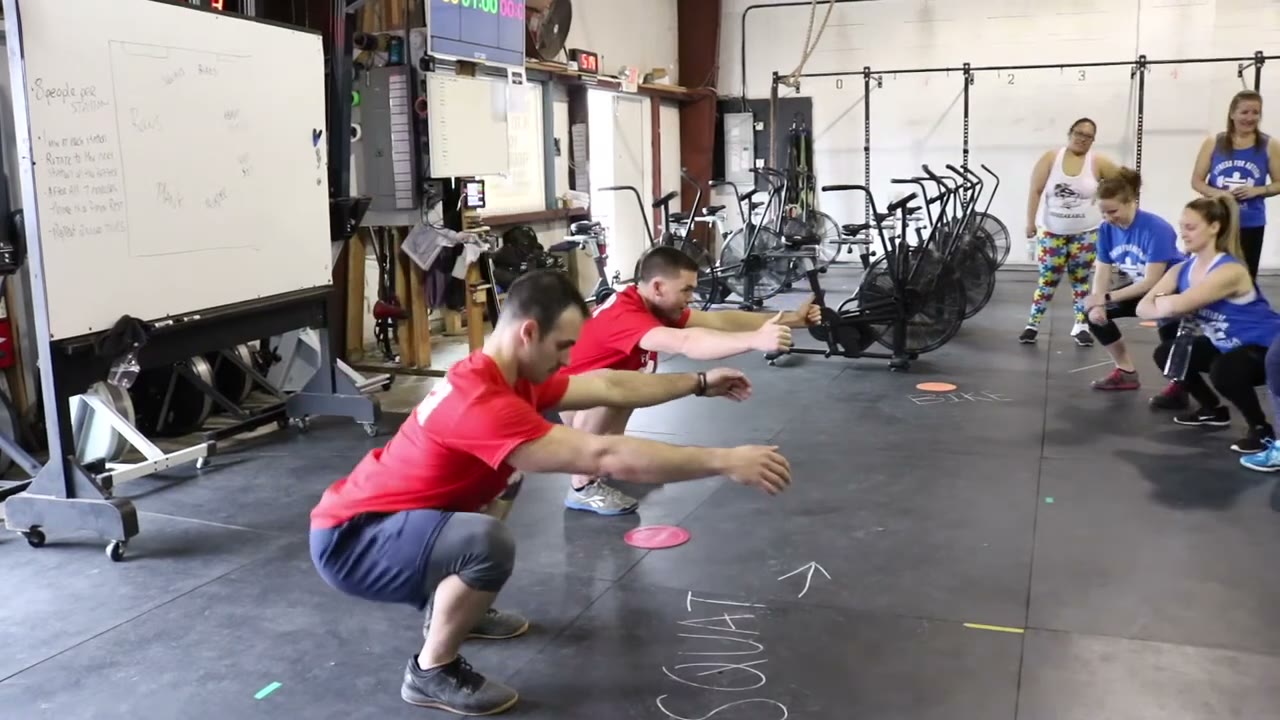 A coach demonstrating a squat while the member line follows along
